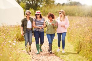 Group,Of,Mature,Female,Friends,Walking,Along,Path,Through,Yurt four women walking arm in arm